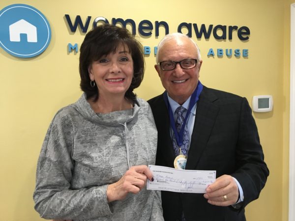 A woman and a man, holding a check and smiling in front a blue logo that reads